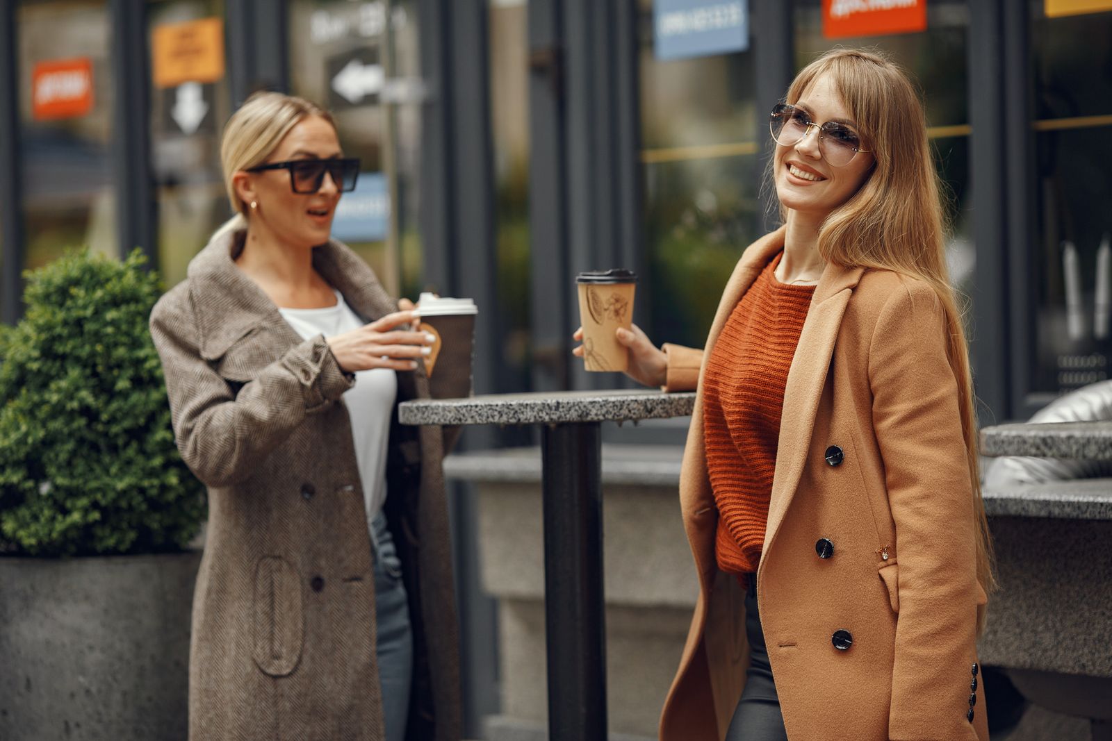 Deux femmes en manteau discutent autour d’un café, dans la rue