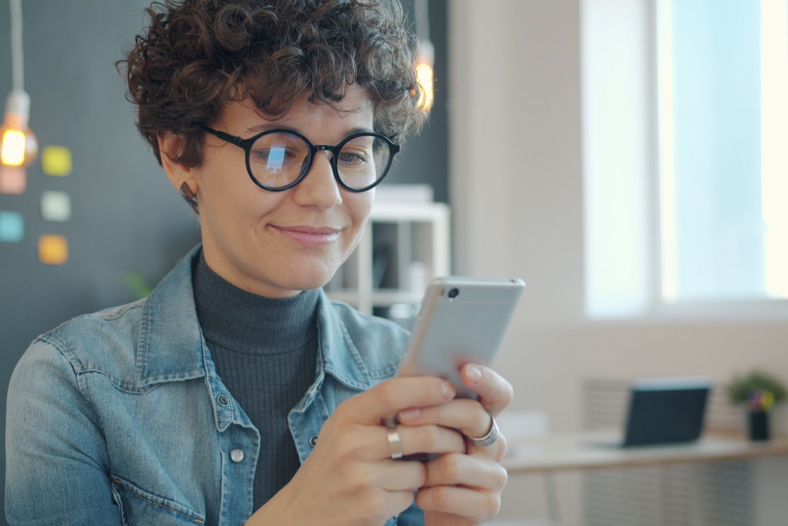 Une femme à lunettes sourit en regardant son téléphone